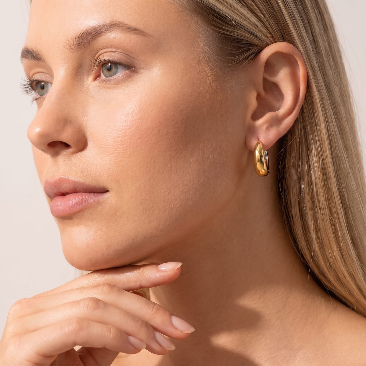 Woman wearing the Nina dome huggie two-tone earrings on the ear with her hand at her chin