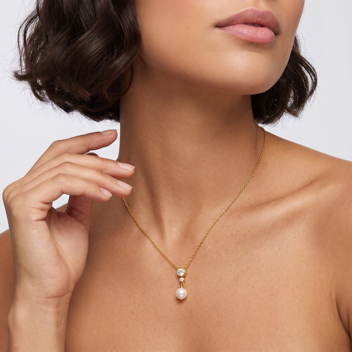 Woman wearing the Odette crystal pearl gold necklace at the collarbone, touching her short hair