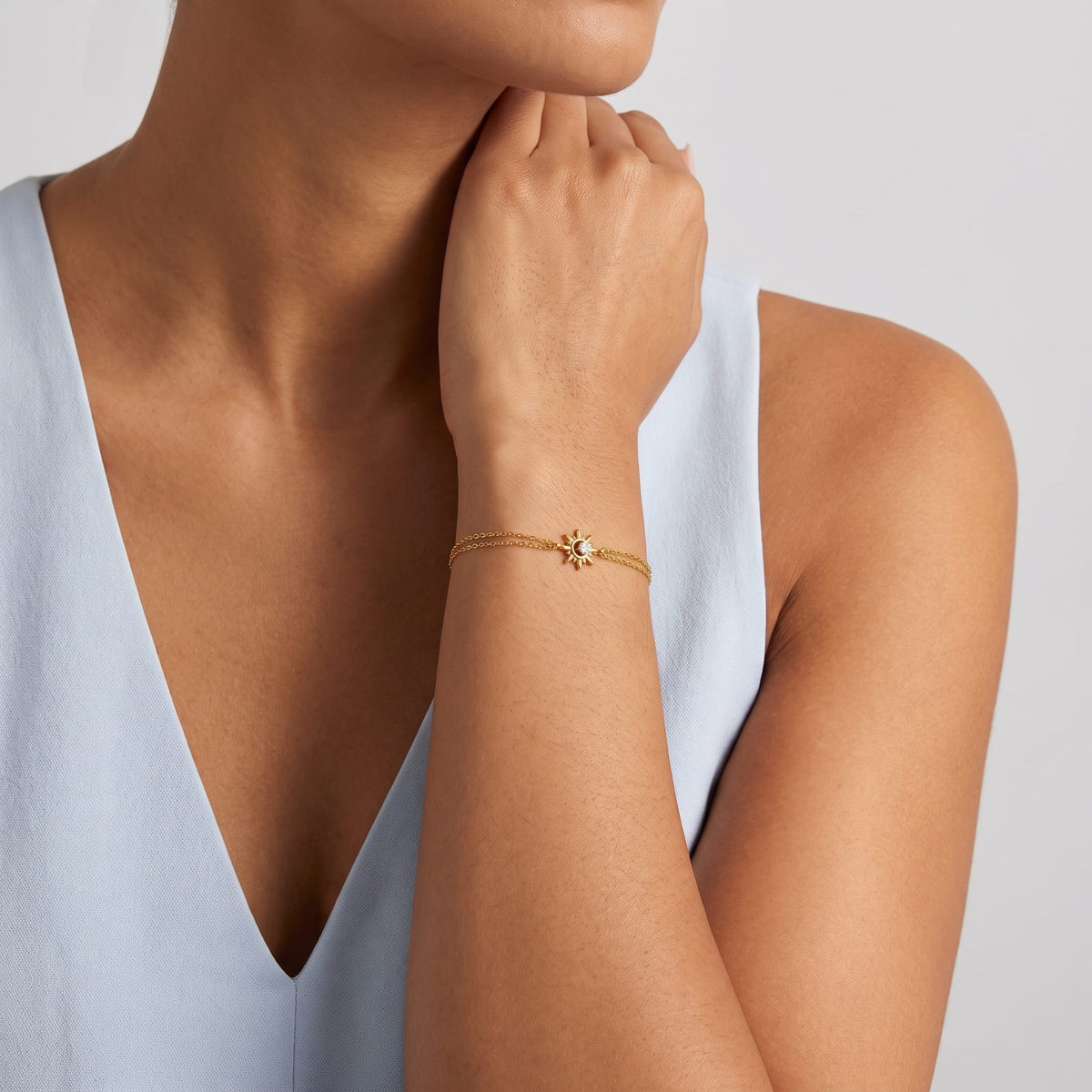 Woman wearing the Olivia crystal sun gold bracelet on the wrist paired with a light blue top