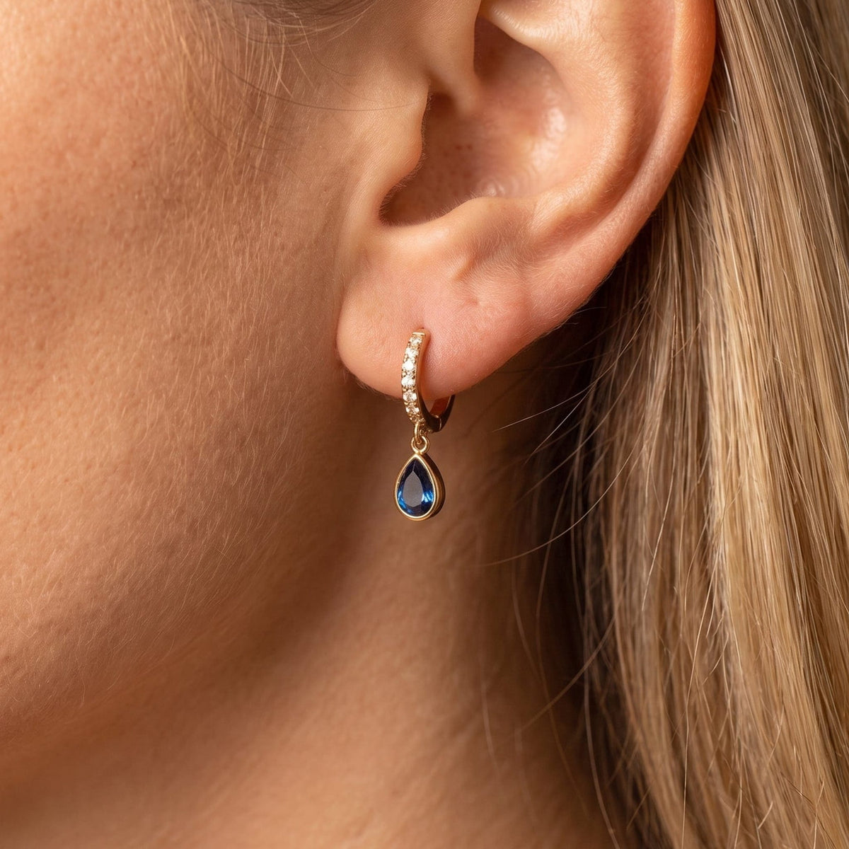 Woman wearing the Paola blue teardrop gold earrings on the ear