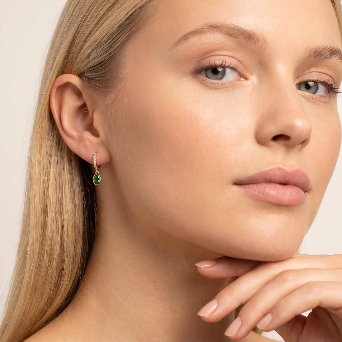 Woman wearing the Paola green oval gold earrings on the ear resting her chin on hand