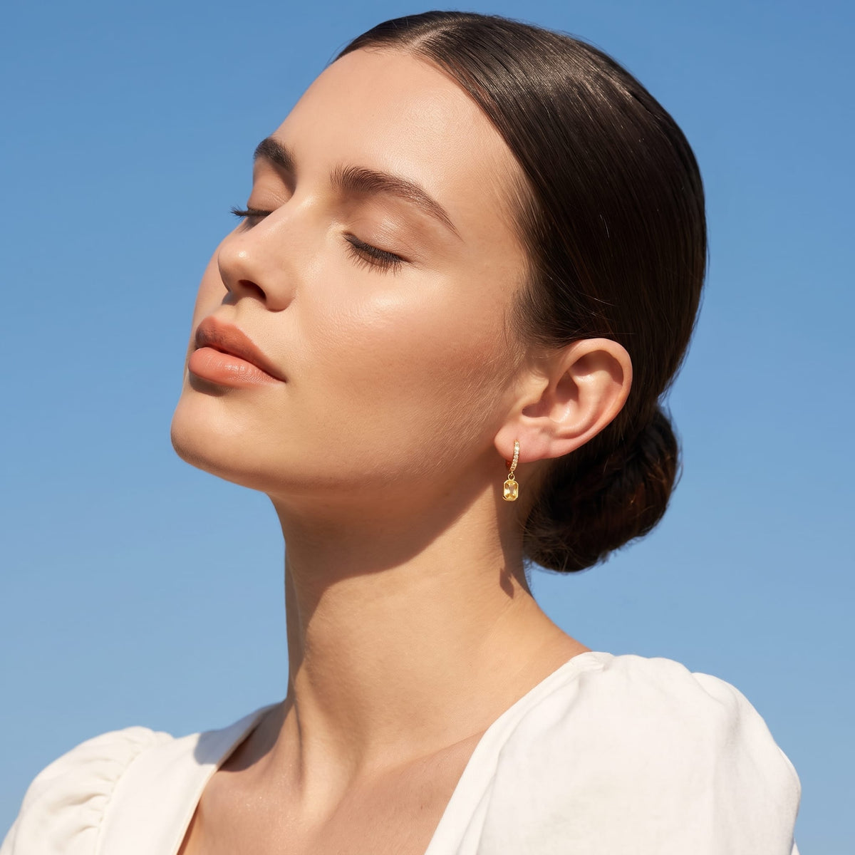 Woman wearing the Paola yellow octagon gold earrings on the ear tilted toward the sun