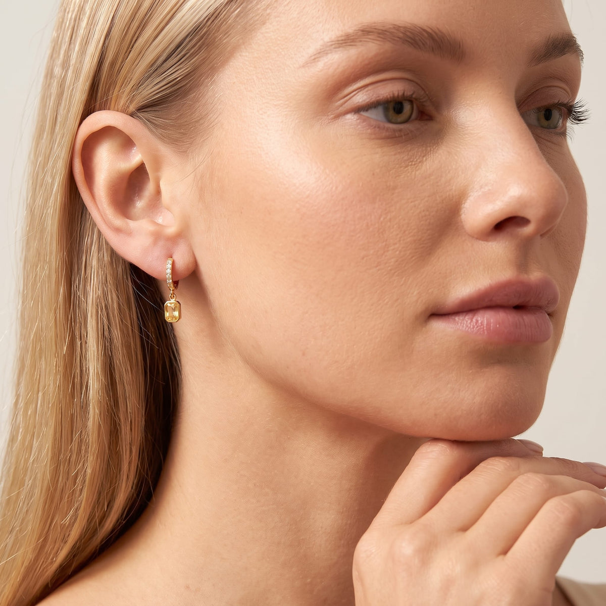 Woman wearing the Paola yellow octagon gold earrings on the ear resting hand on chin