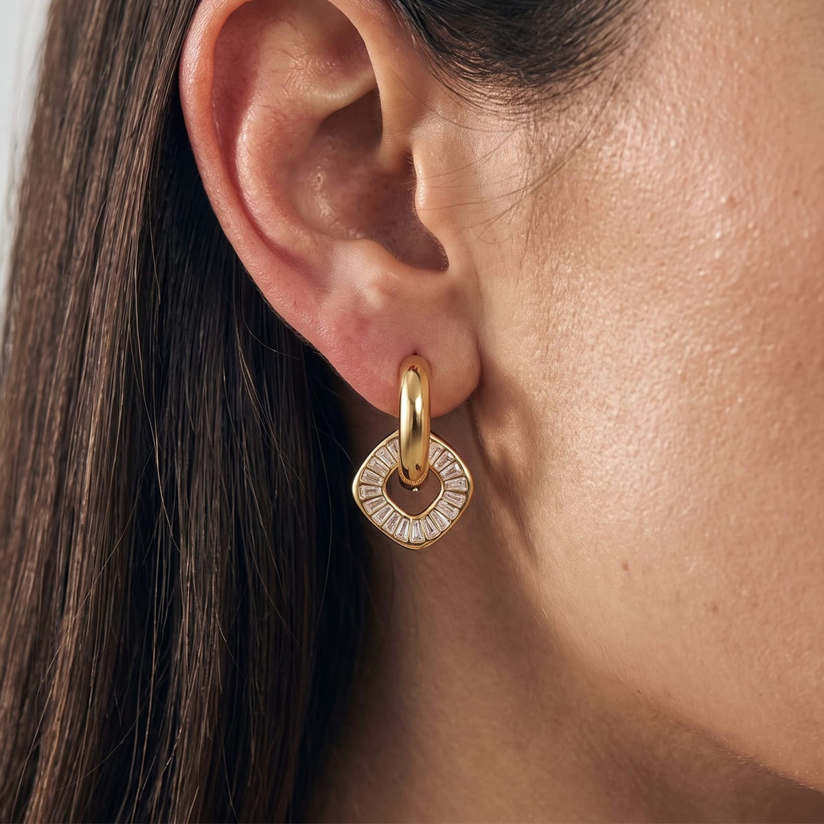 Woman wearing the Salomé baguette charm gold earrings on her earlobe in a close-up view
