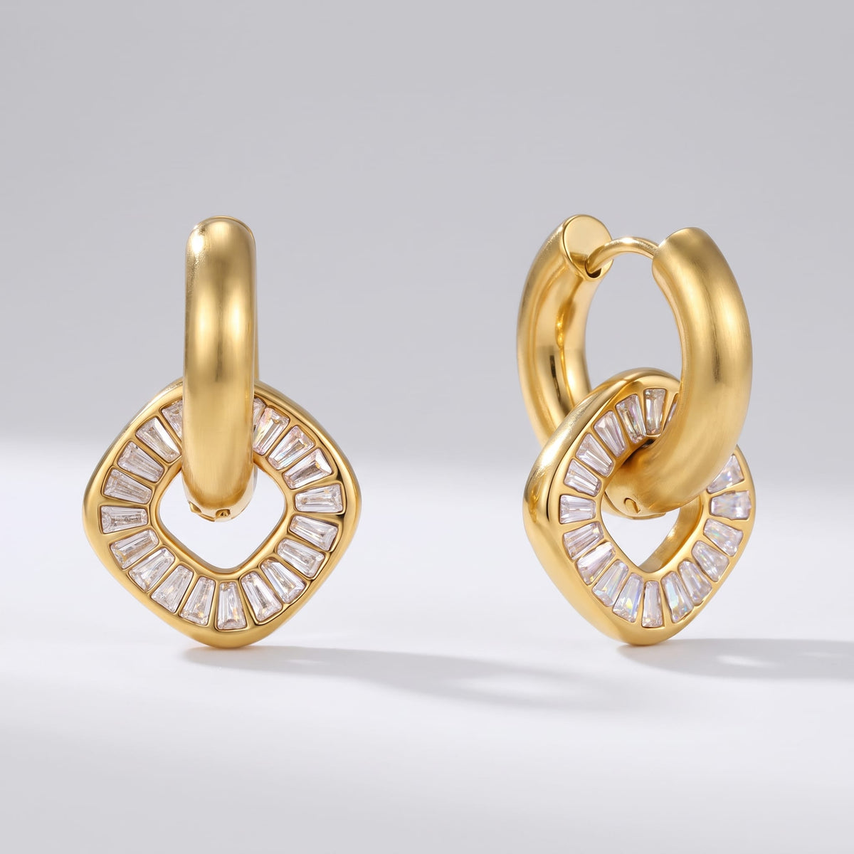 Salomé baguette charm gold earrings on a plain gray surface in studio lighting