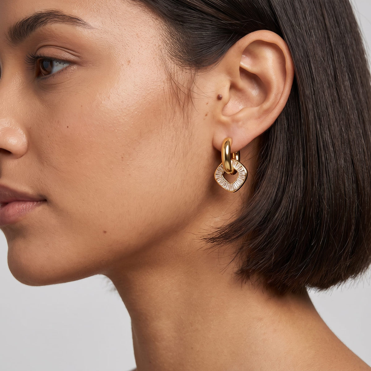 Woman wearing the Salomé baguette charm gold earrings on her ear with short dark hair