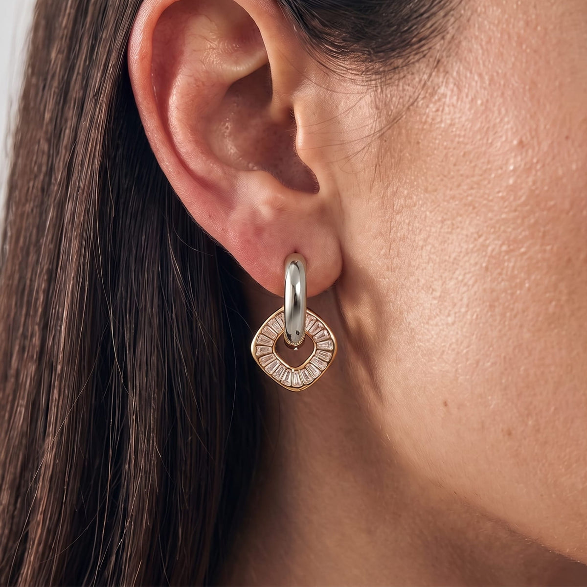 Woman wearing the Salomé baguette charm two-tone earrings on her ear in a close-up profile shot