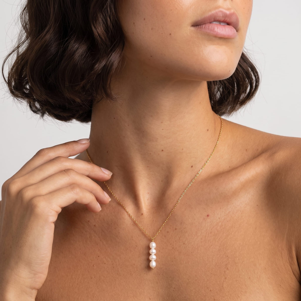 Woman wearing the Simone stacked pearl gold necklace at the collarbone with her hand raised near her chin