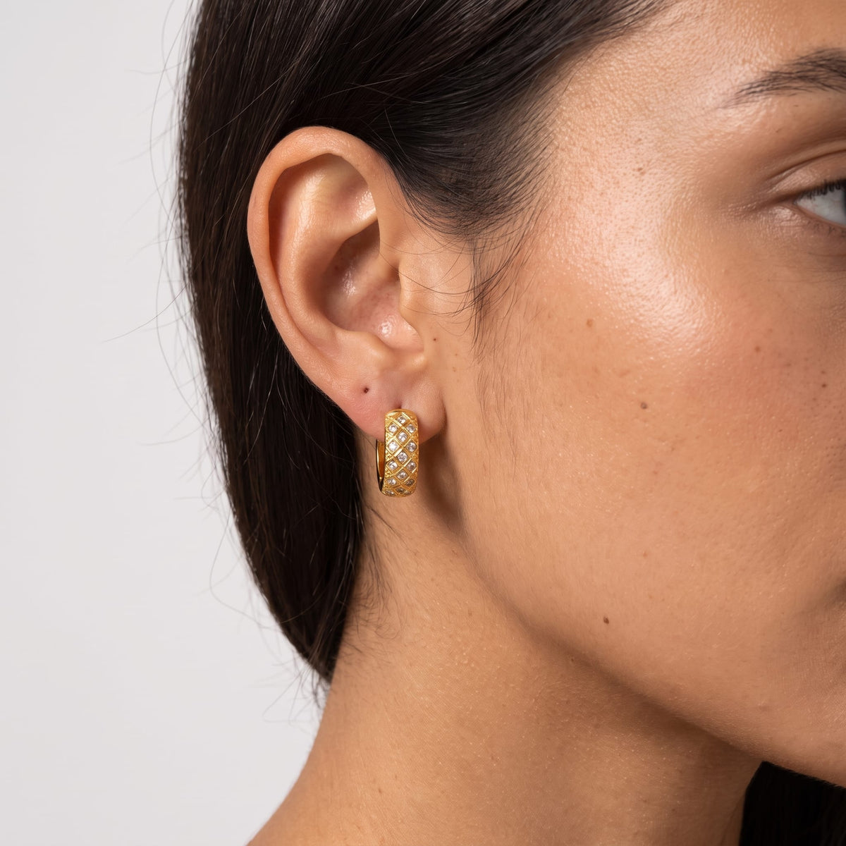 Woman wearing the Solène lattice hoop gold earrings on her earlobe in a close cropped view