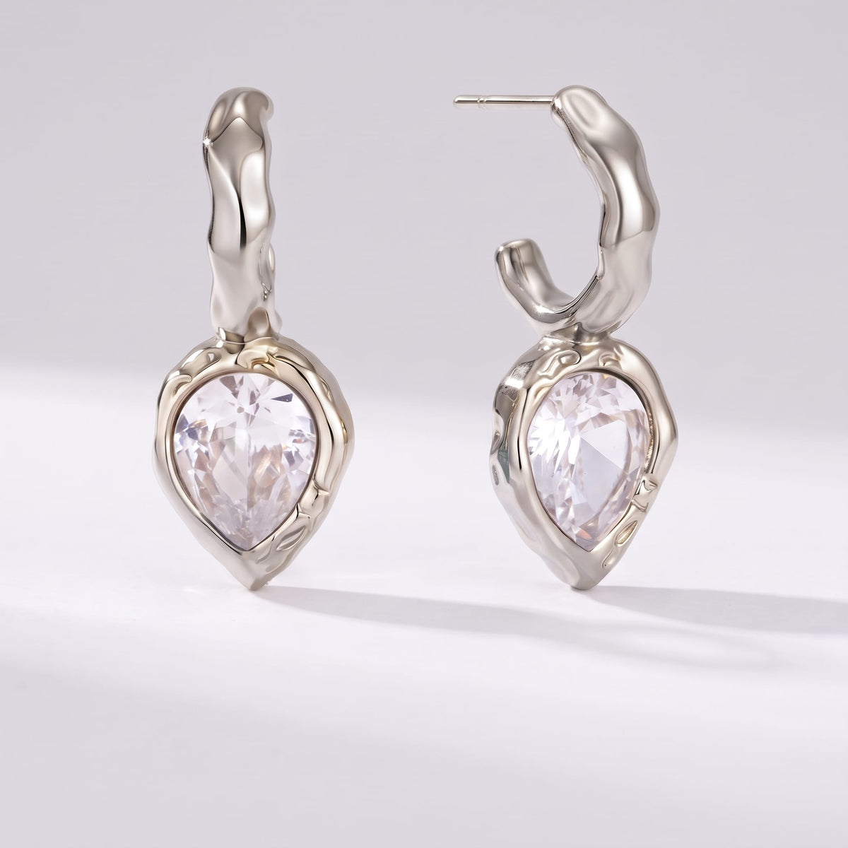 Victoire hammered teardrop silver earrings on a plain light grey surface