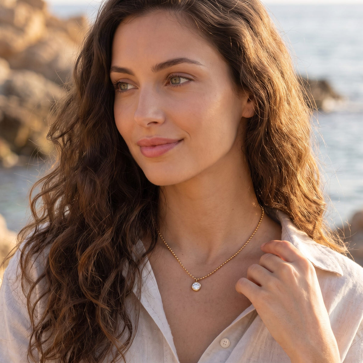 Woman by the sea at golden hour wearing the Vida crystal bezel gold necklace