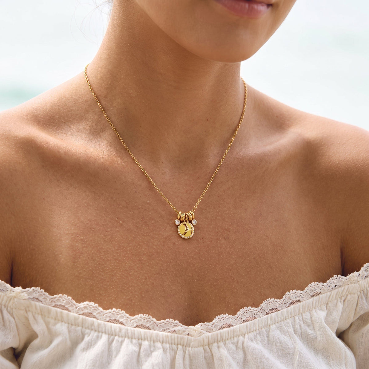 Wider view of a woman wearing the Vida softball charm gold necklace at the collarbone
