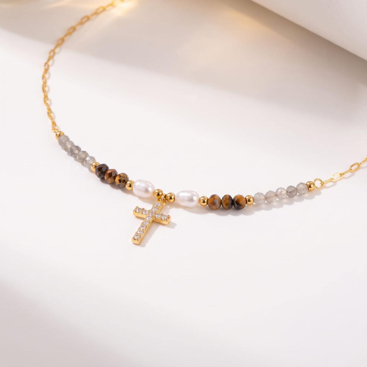 Viola pearl cross gold necklace on a white surface with soft light and shadows