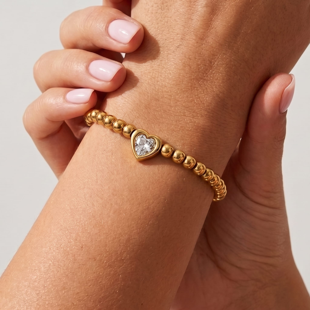 Woman wearing the Vittoria gold beaded bracelet with a heart-cut crystal in the center