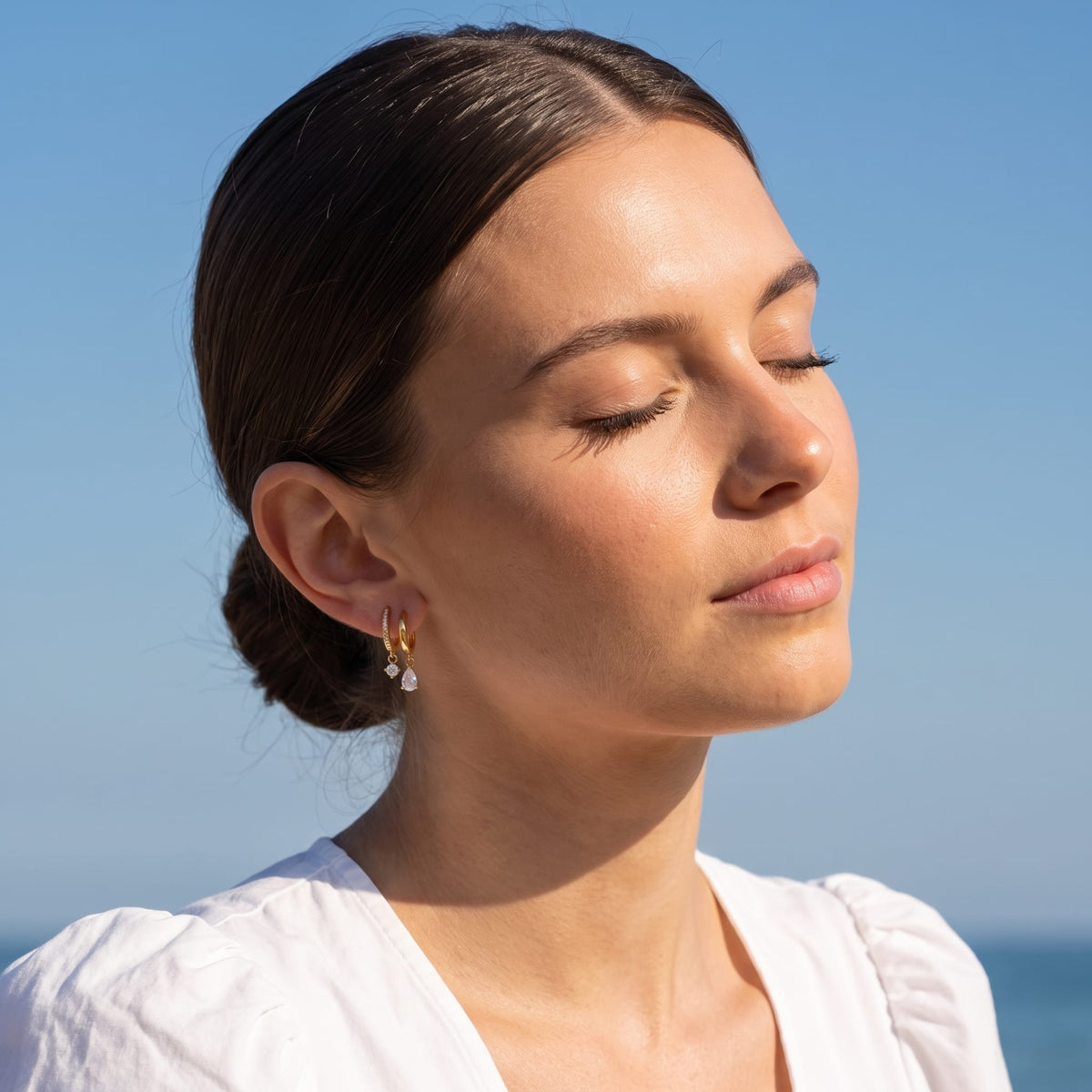 Woman wearing the Ysaline double hoop gold earrings on her ear under a bright blue sky