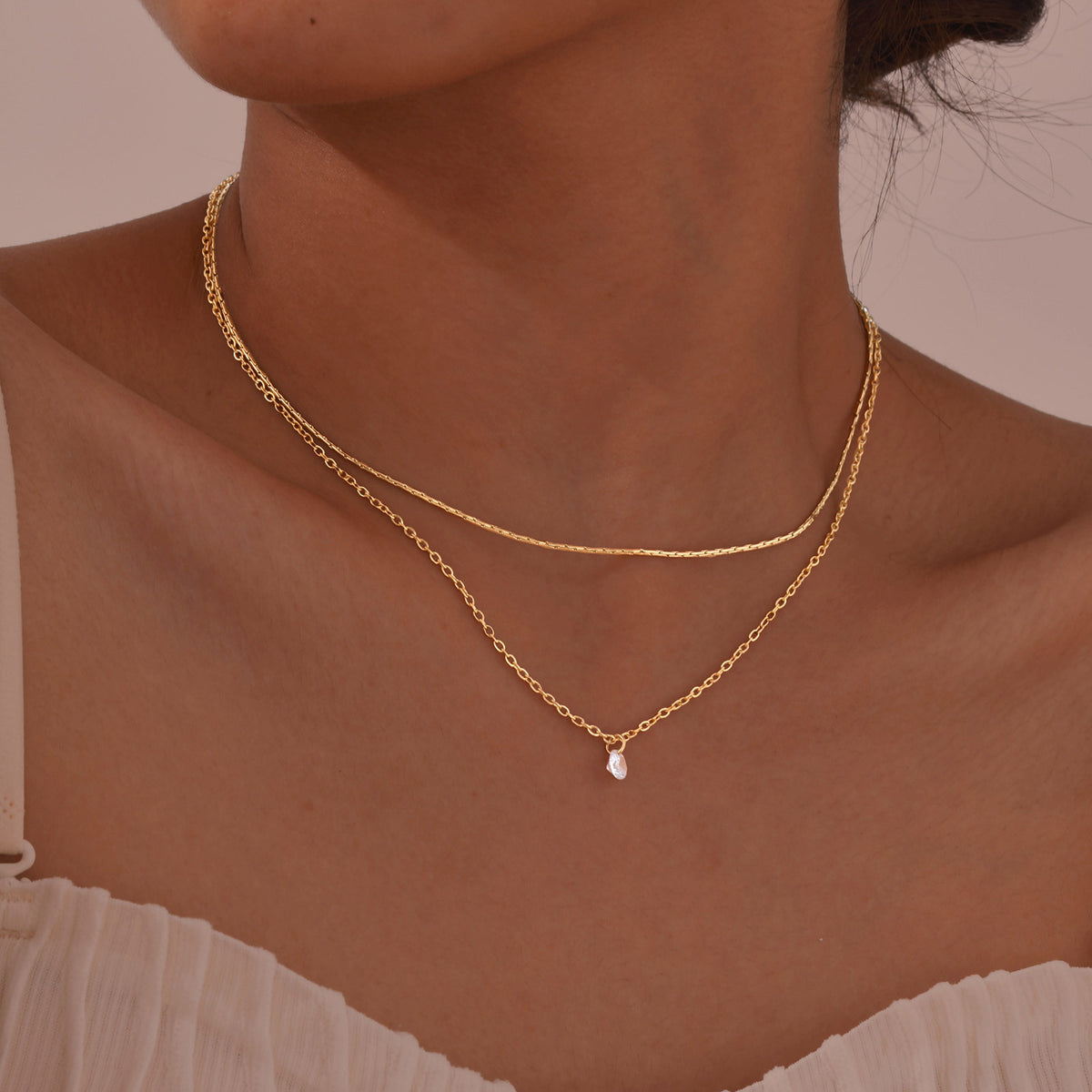 Woman wearing the Lora two-layer gold necklace, a fine chain above a cable chain with a tiny drop