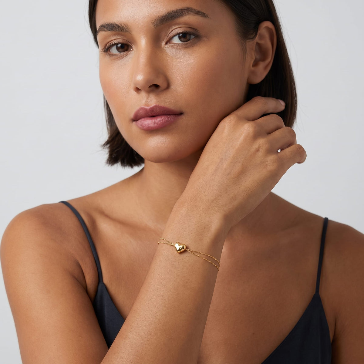 Woman wearing the Adèle hammered heart gold bracelet on the wrist posing against a neutral backdrop