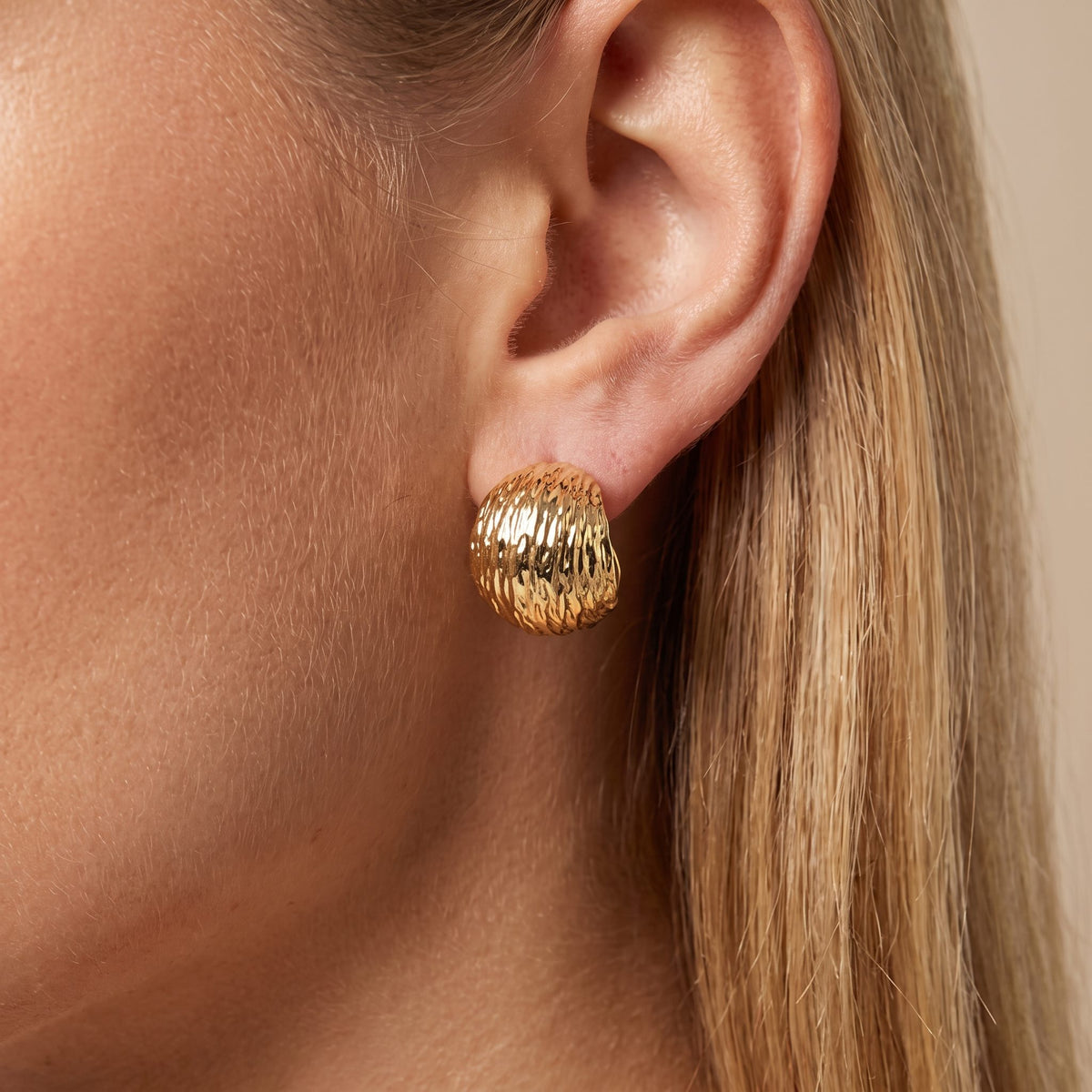 Woman wearing the Alexa gold earring, a ribbed domed stud sitting on the lobe