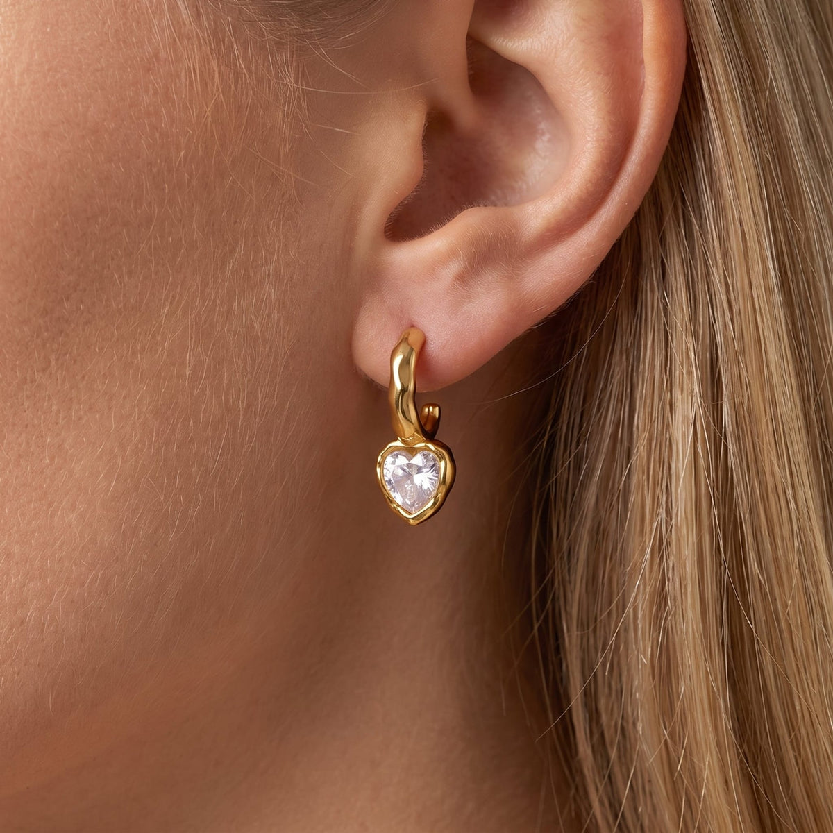 Woman wearing the Amandine hammered heart gold earrings on the ear, featuring a heart-shaped crystal