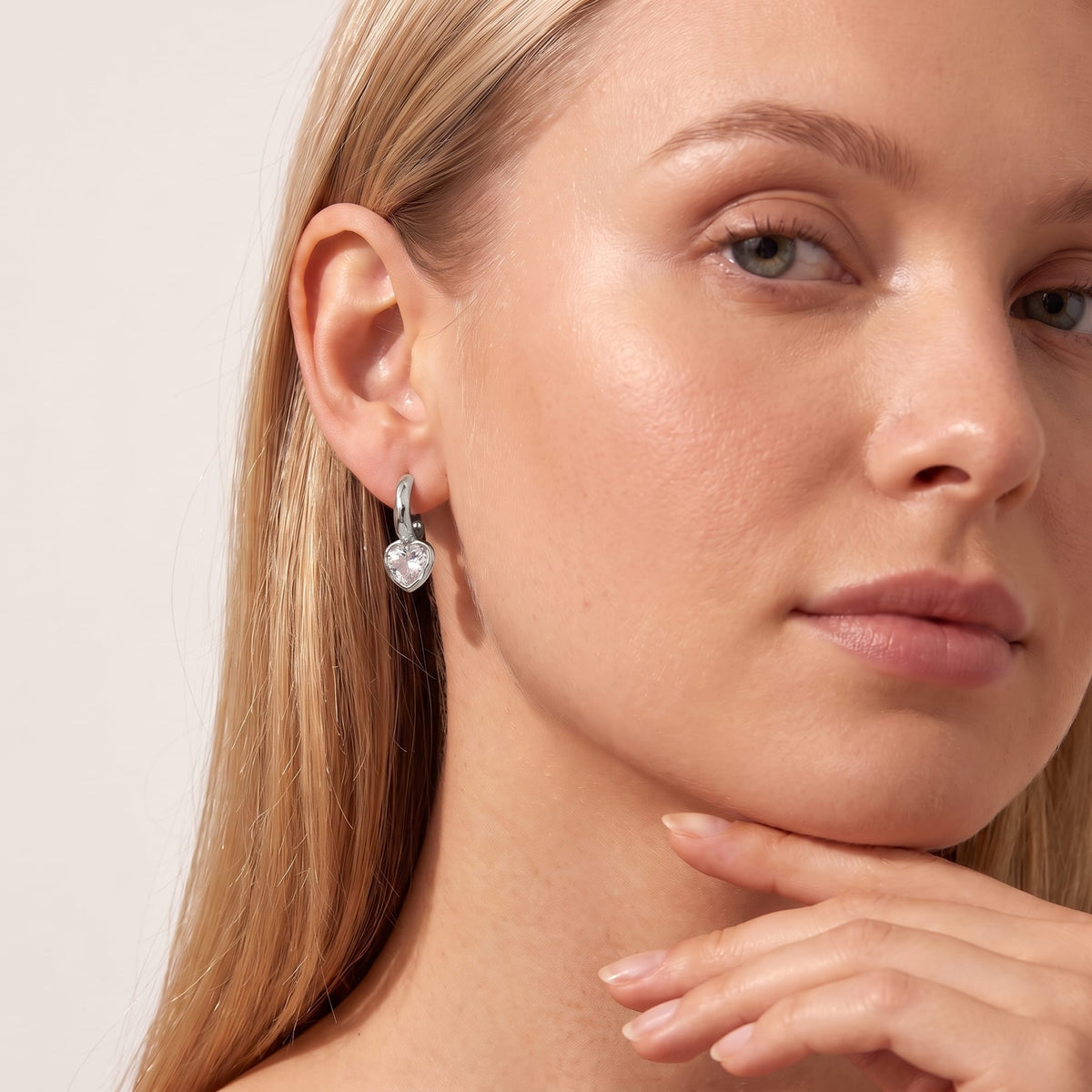 Woman wearing the Amandine hammered heart silver earrings on her ear resting her chin on her hand