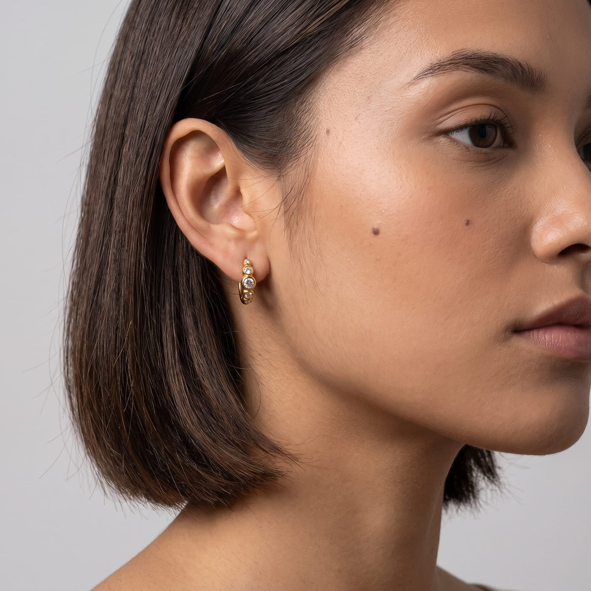 Woman wearing the Anaïs crystal huggie gold earrings on her earlobe showing her short dark bob haircut