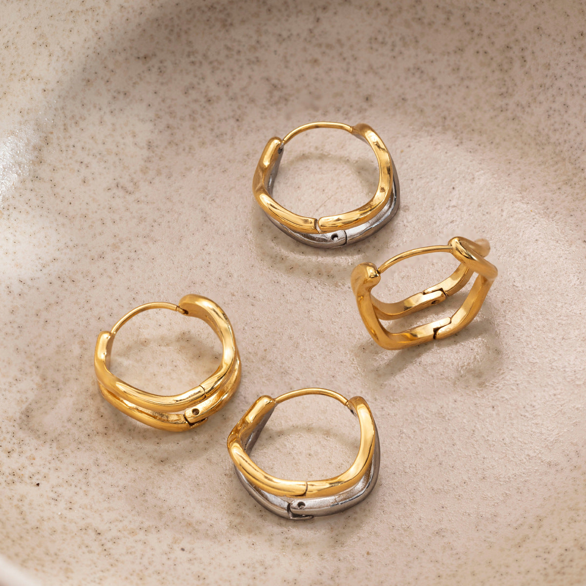 Gold and two-tone Anouk wave hoops lying open in a speckled stoneware dish