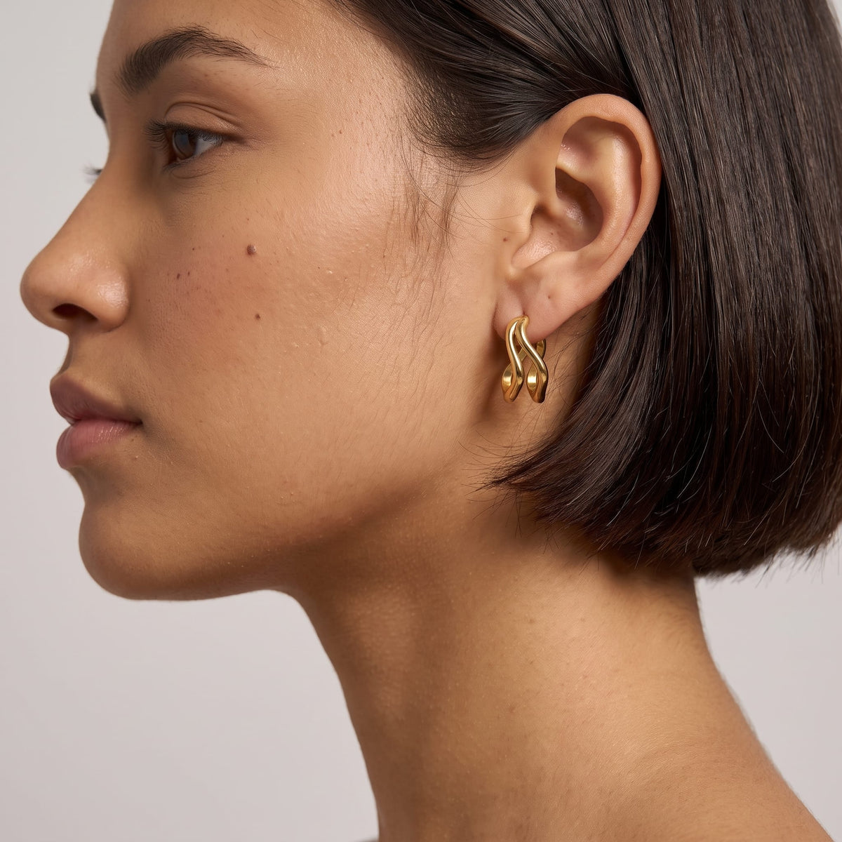 Woman wearing the Anouk double wave gold earrings on the ear with a brunette short bob haircut