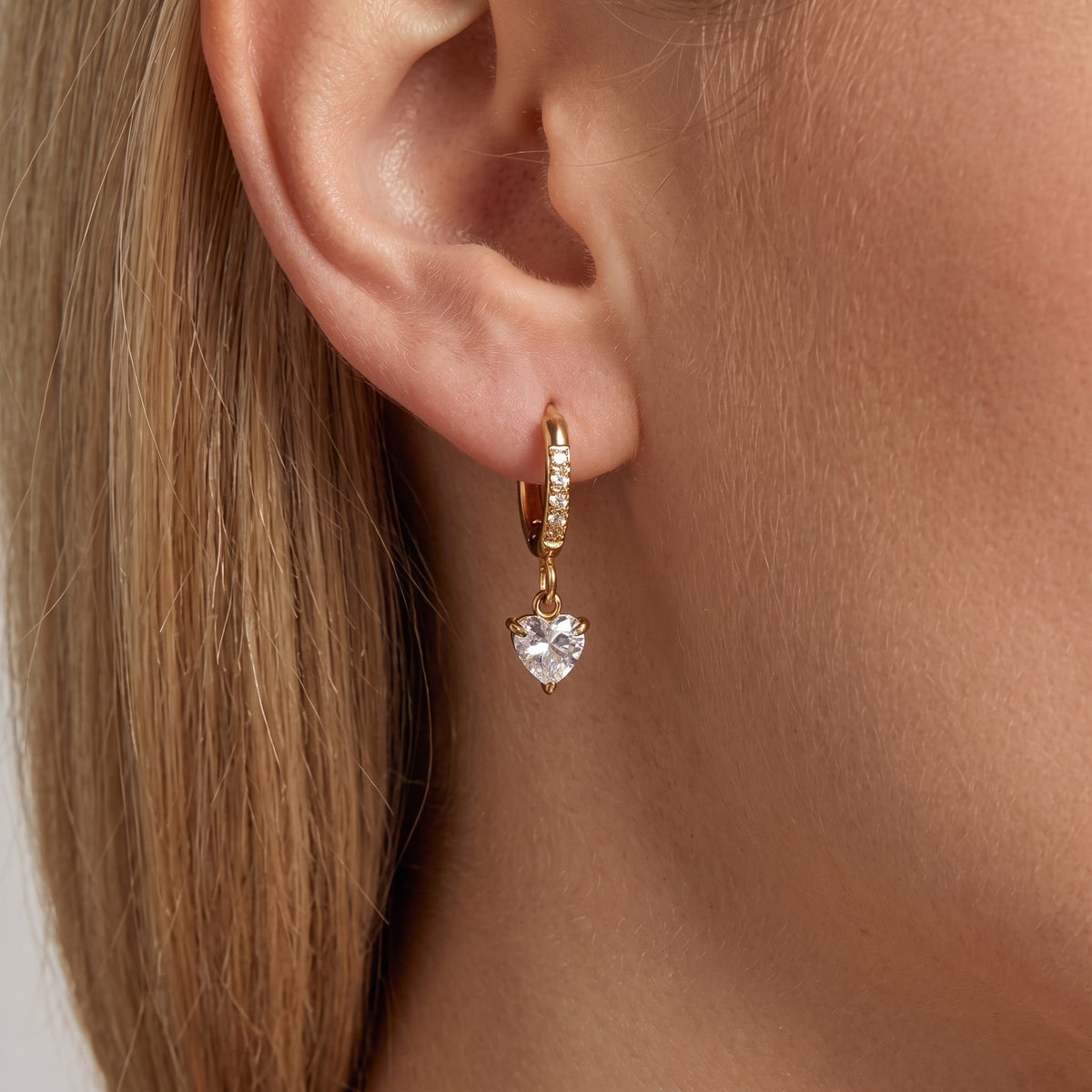 Woman wearing an Aurélie gold pavé huggie with a clear crystal heart drop on the ear