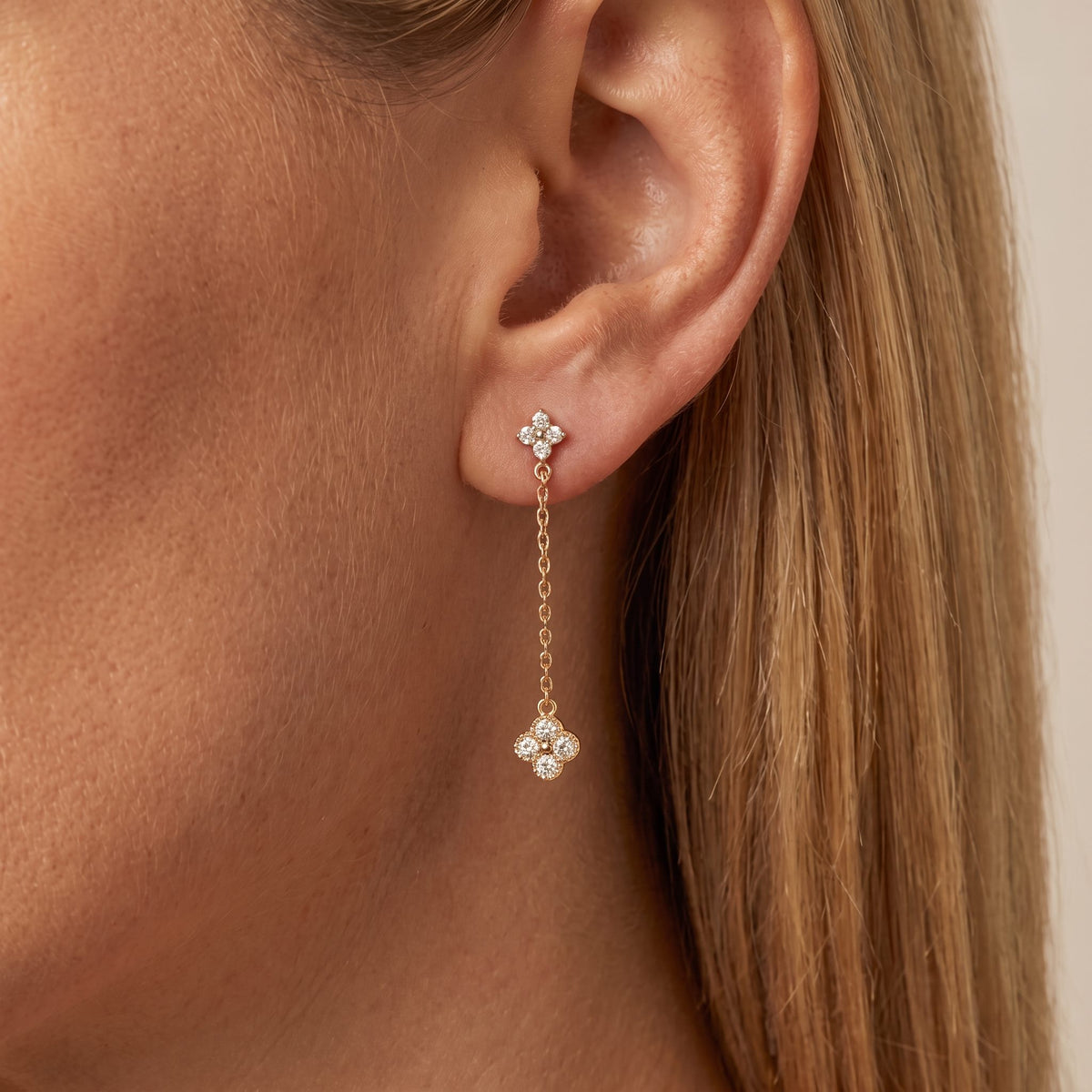 Woman wearing an Aurélie gold drop earring, a crystal clover stud with a larger clover on a fine chain