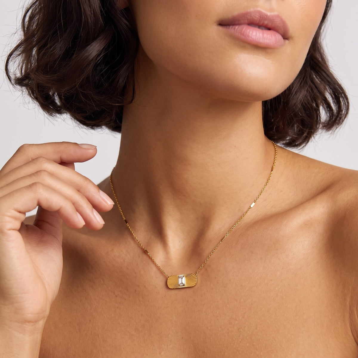 Woman wearing the Aurora sunburst crystal gold necklace at the collarbone while touching her hair