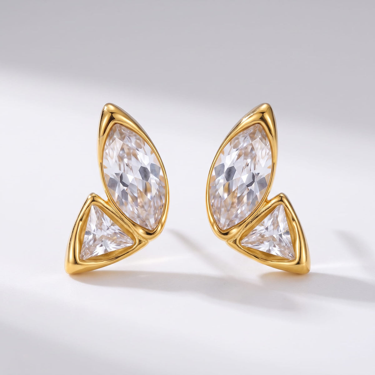 Aurore crystal wing gold earrings on a plain white studio surface