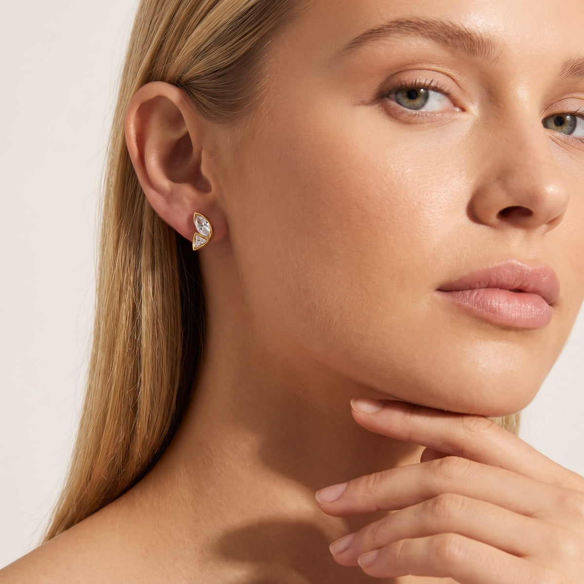 Woman wearing the Aurore crystal wing gold earrings on her ear, touching her chin with blonde hair
