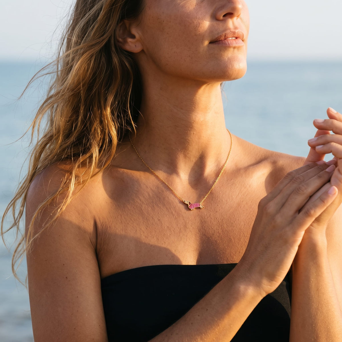 Woman wearing the Bianca pink dachshund gold necklace at the collarbone in warm outdoor sunlight