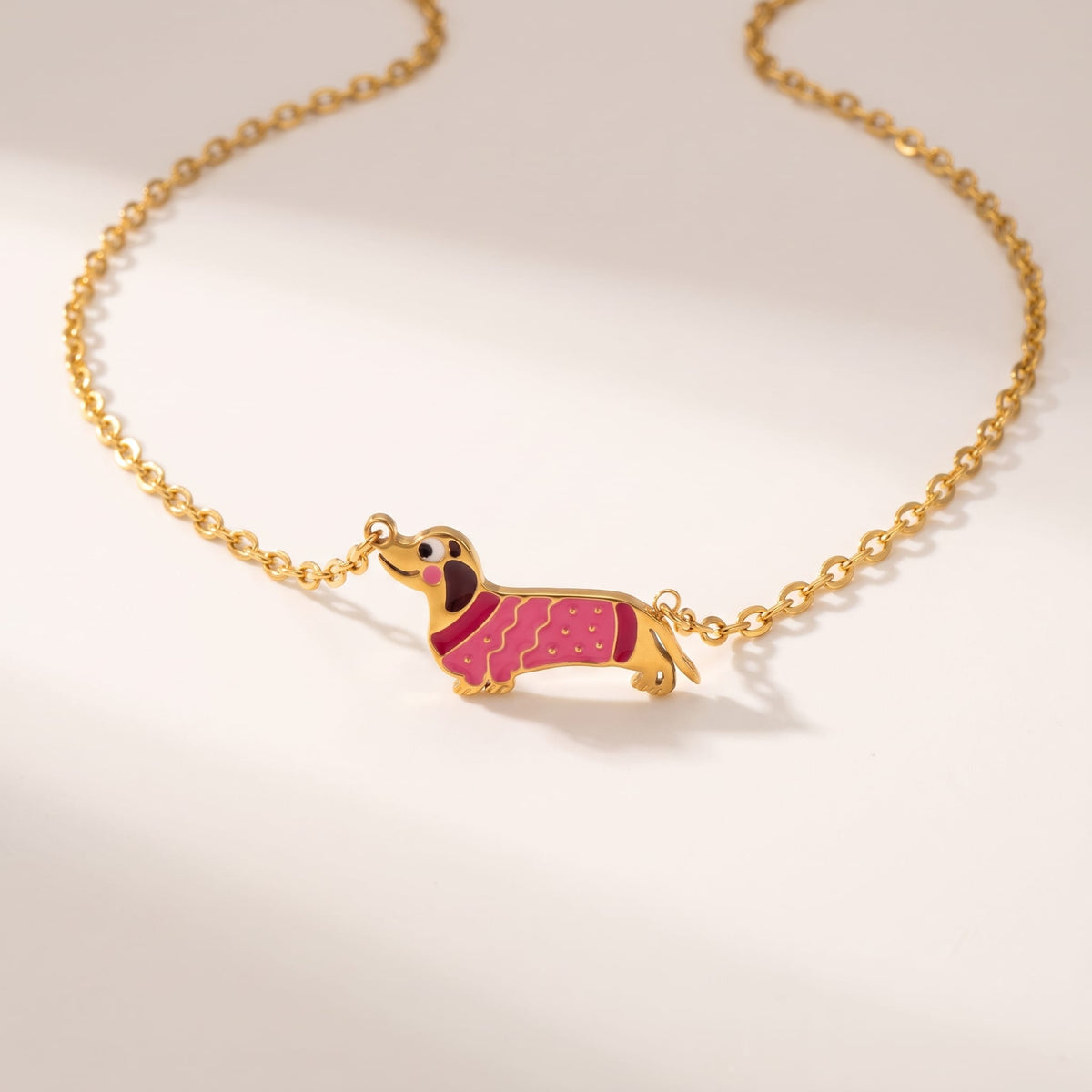 Bianca pink dachshund gold necklace on a white surface with gentle shadows