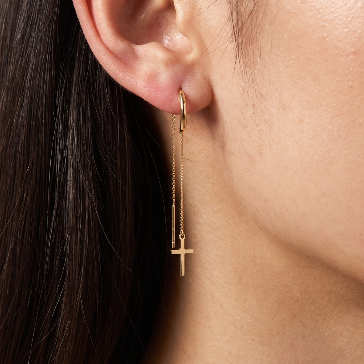 Woman with long dark hair wearing the Camille gold threader earring with a small cross charm