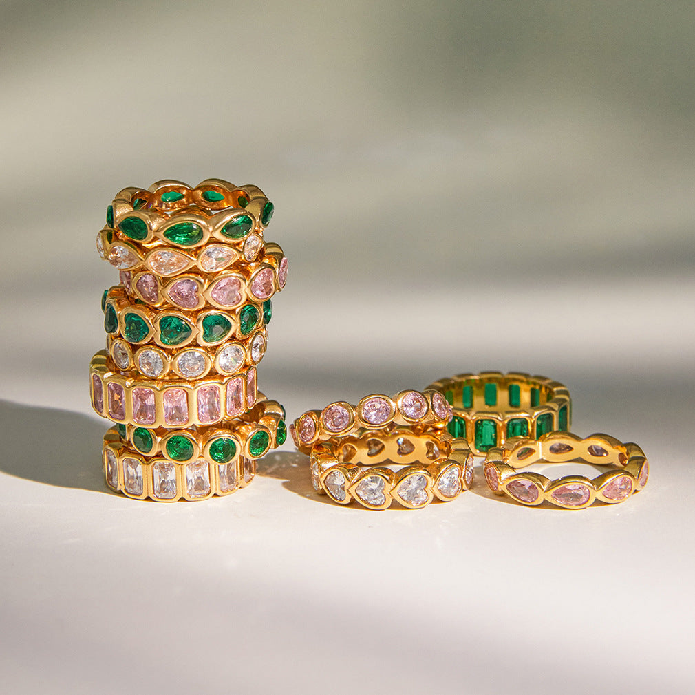 Stacks of crystal eternity rings in clear, pink and green on a pale surface