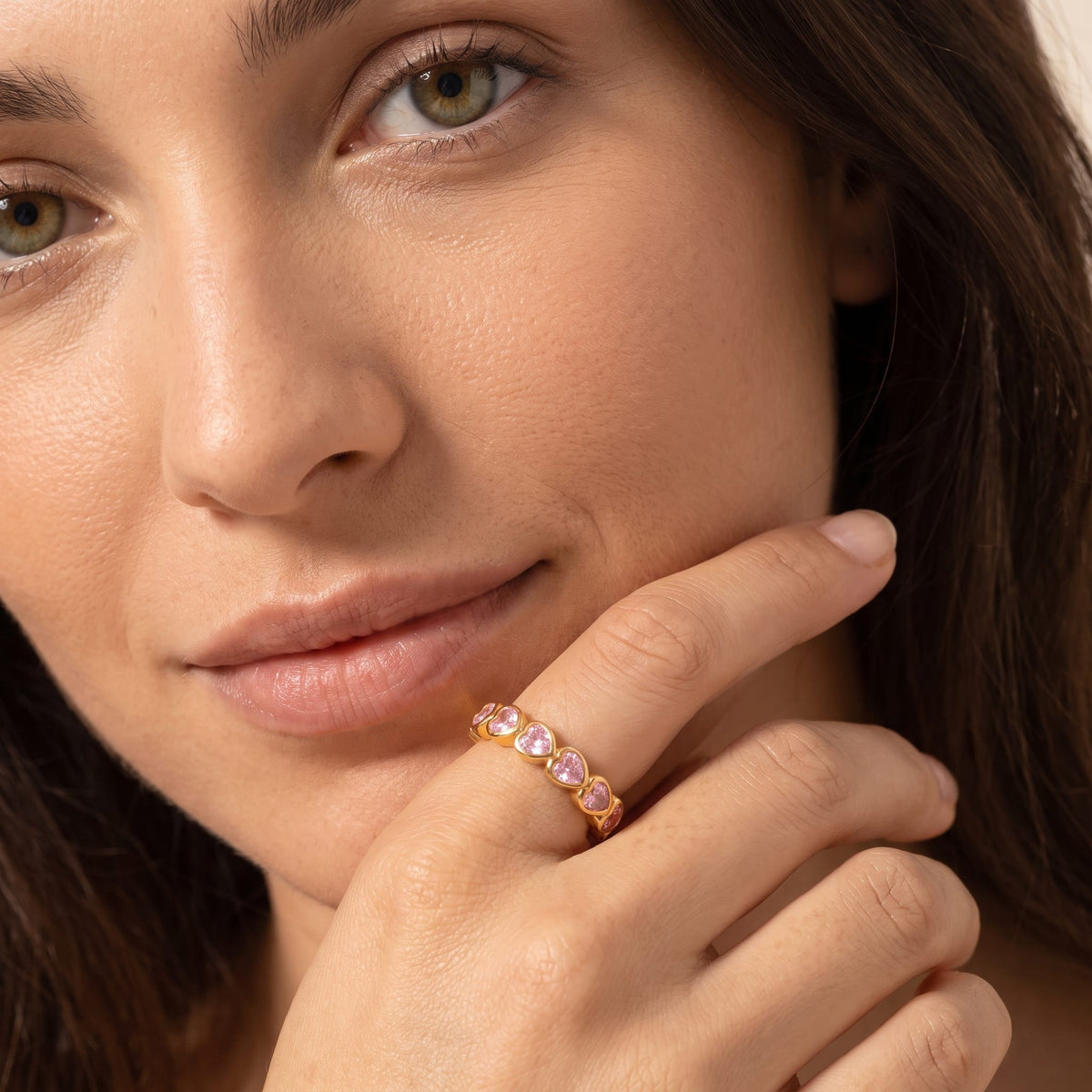 Woman wearing the Camille pink heart gold ring on the hand resting near her chin