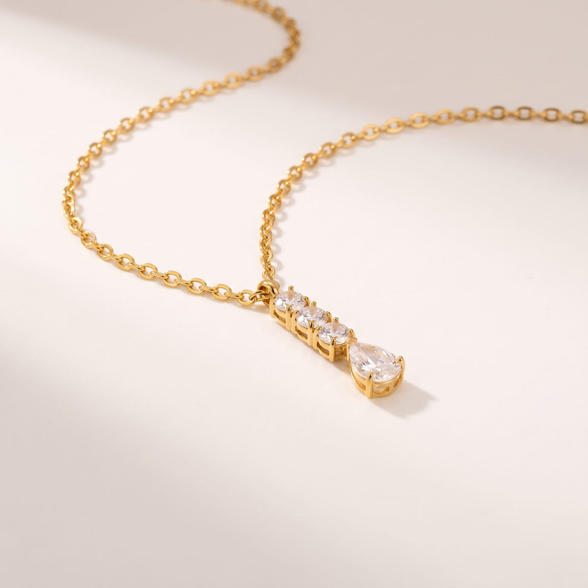 Close-up of the Céleste pear drop gold necklace on an off-white surface