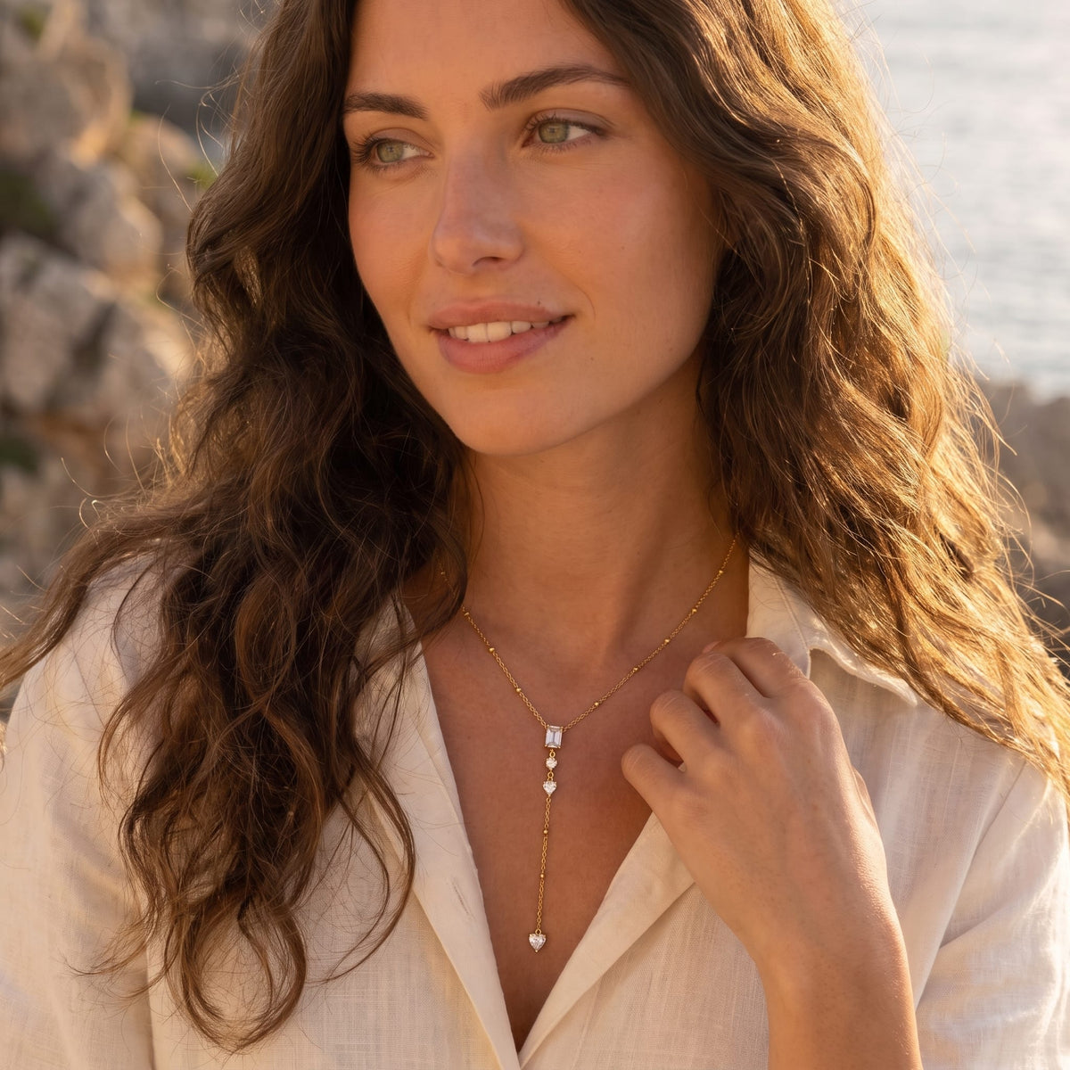 Woman wearing the Constance emerald-cut lariat gold necklace at the collarbone in a white linen shirt