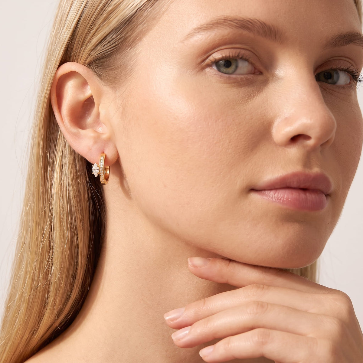Woman wearing the Diletta marquise huggie gold earrings on the ear with hand on chin