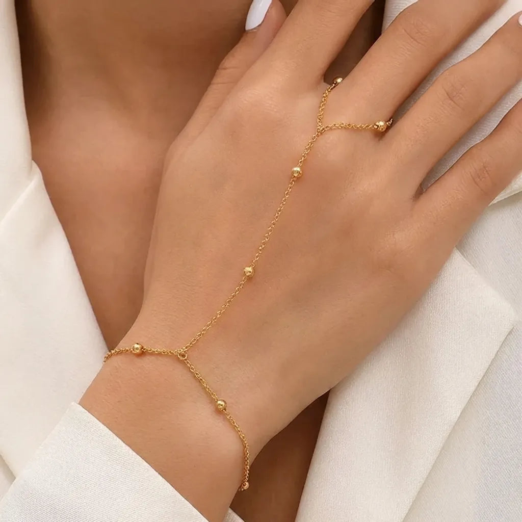Evelyne Fine gold hand chain with small polished beads worn on the hand against a white blazer