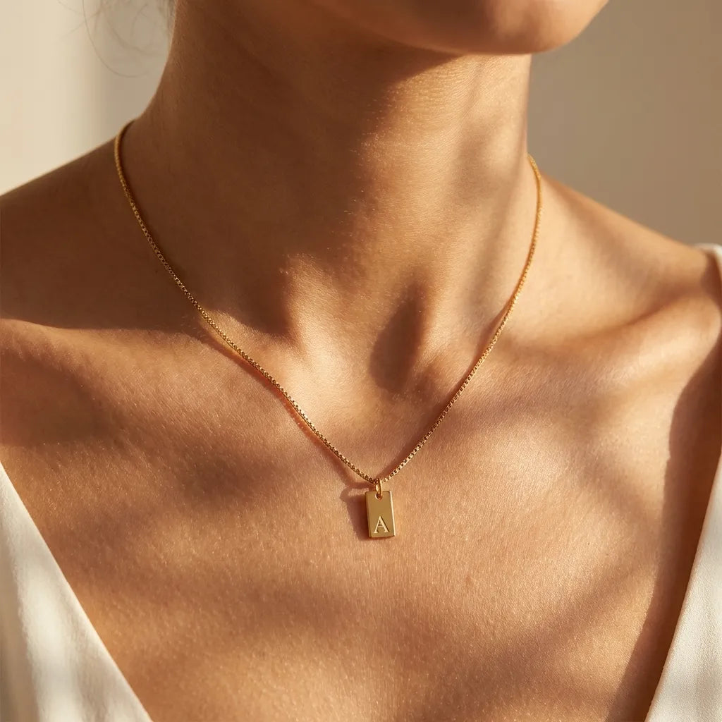 Woman wearing the Chloé initial necklace, a gold rectangular tag engraved A on a box chain