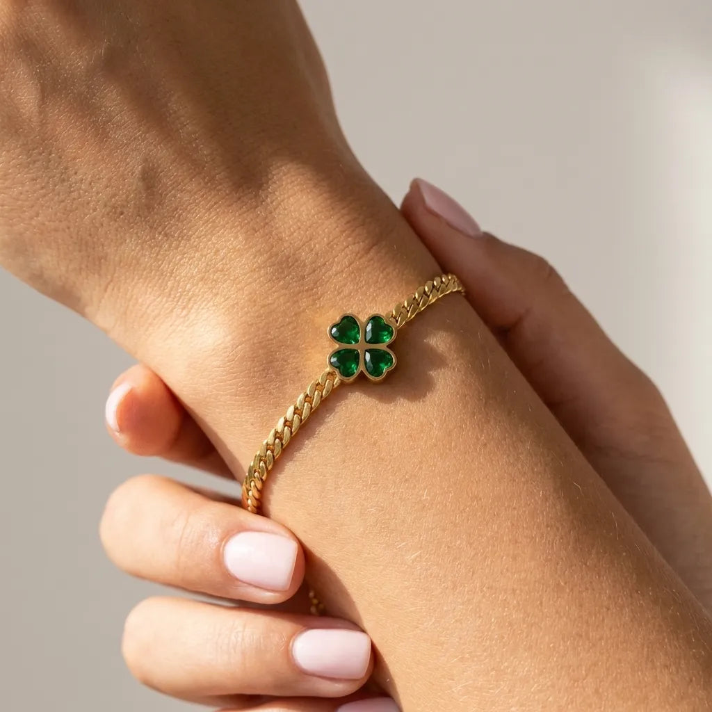 Gold curb chain bracelet with a green crystal heart clover charm worn on the wrist