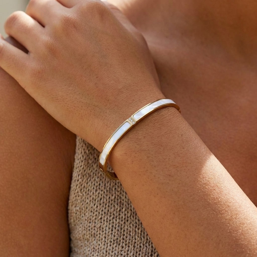 Sarah gold bangle with a white inlay worn on the wrist over a knit top