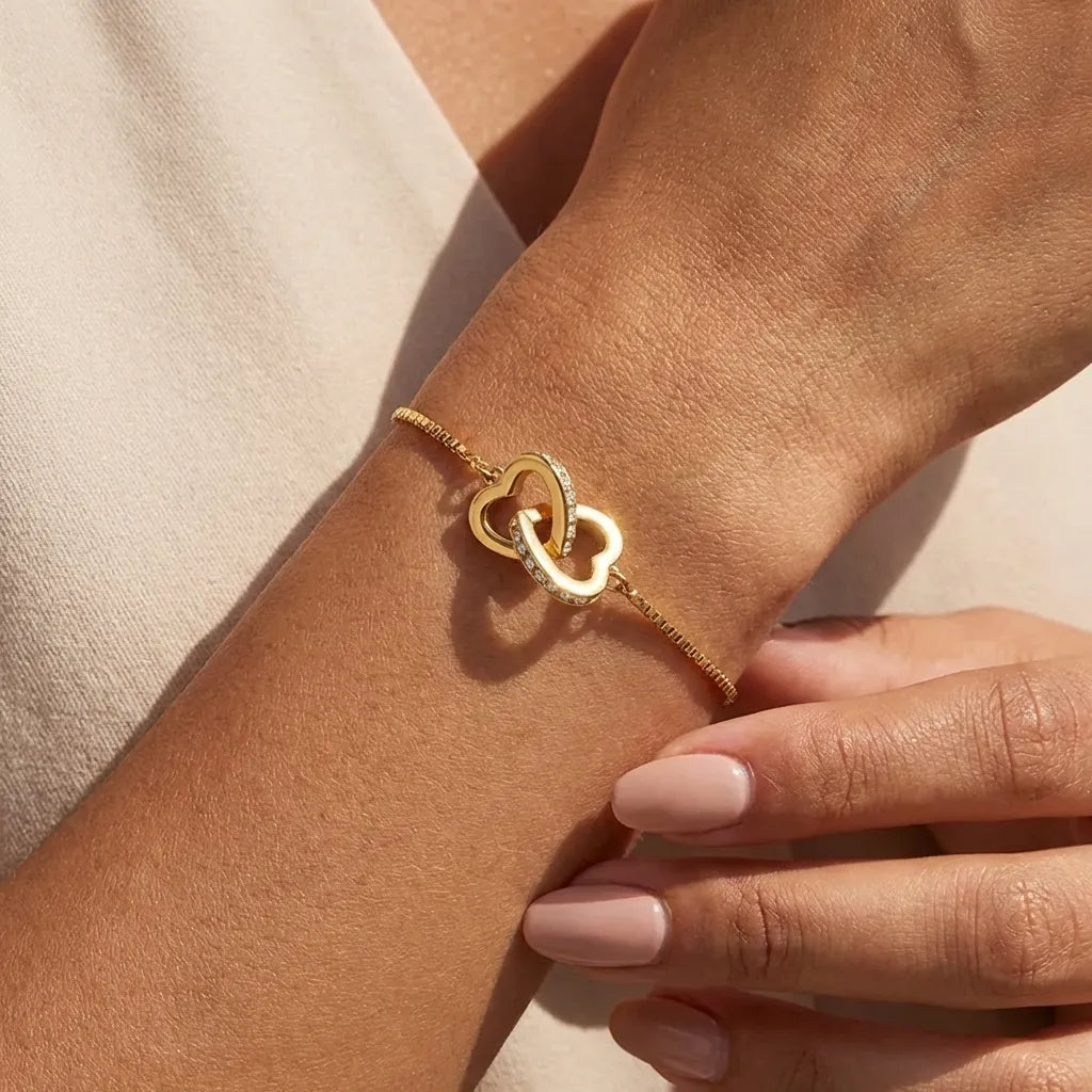Sofia linked hearts bracelet in gold on the wrist, one plain and one crystal-lined heart interlocked
