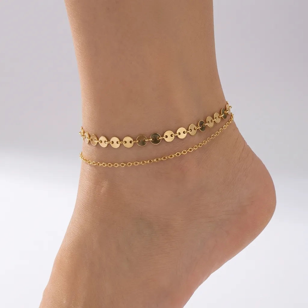 Eliane disc anklet in gold, a flat disc chain layered above a fine cable chain on the ankle