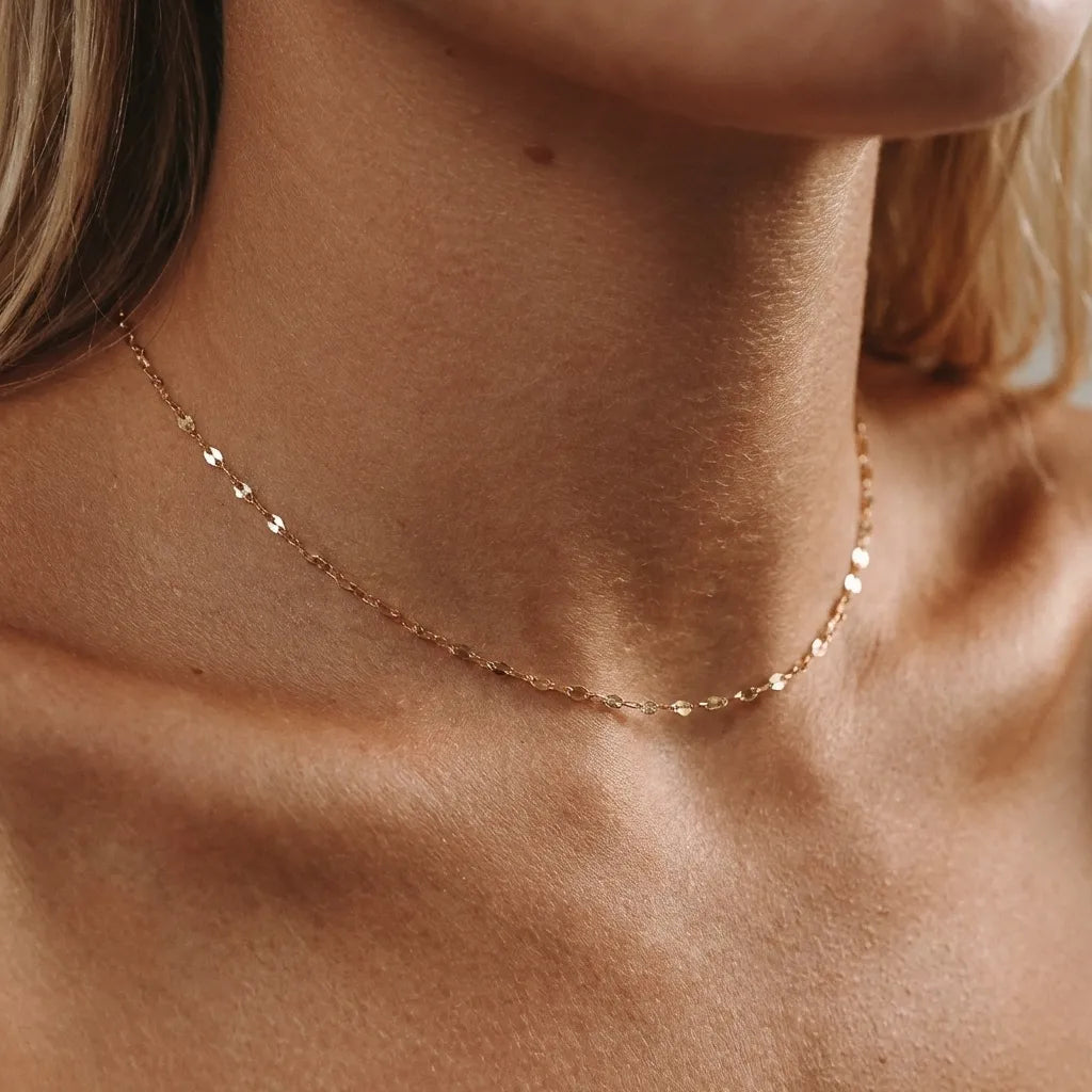 Close view of the Amara gold choker, a fine chain of flat sparkling links at the throat