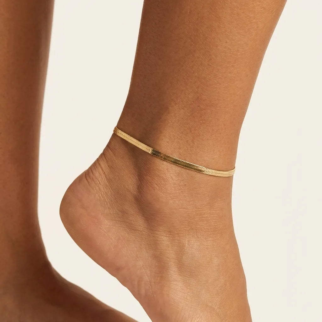 Woman wearing the Gia gold herringbone anklet, a single flat and smooth chain, on the ankle