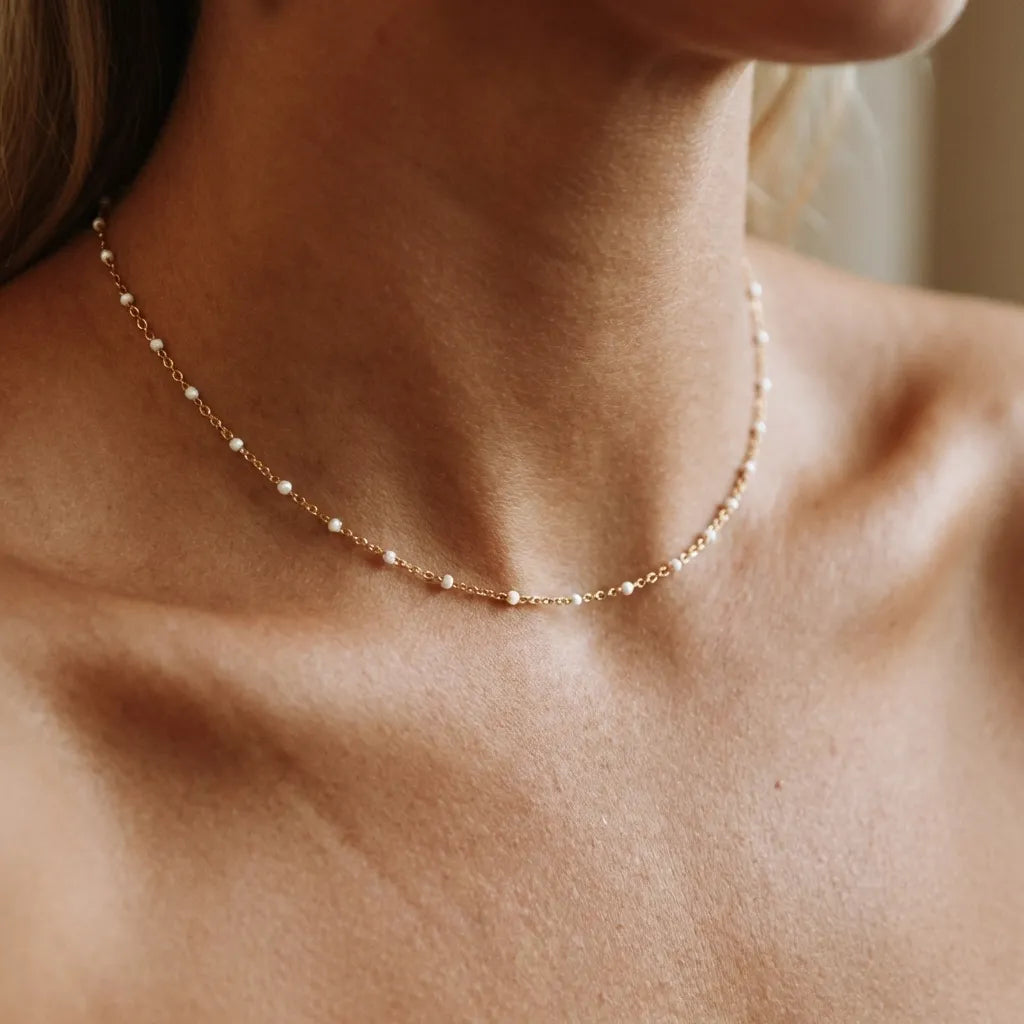 Woman wearing the Fiona gold beaded necklace with tiny white enamel dots close around the neck