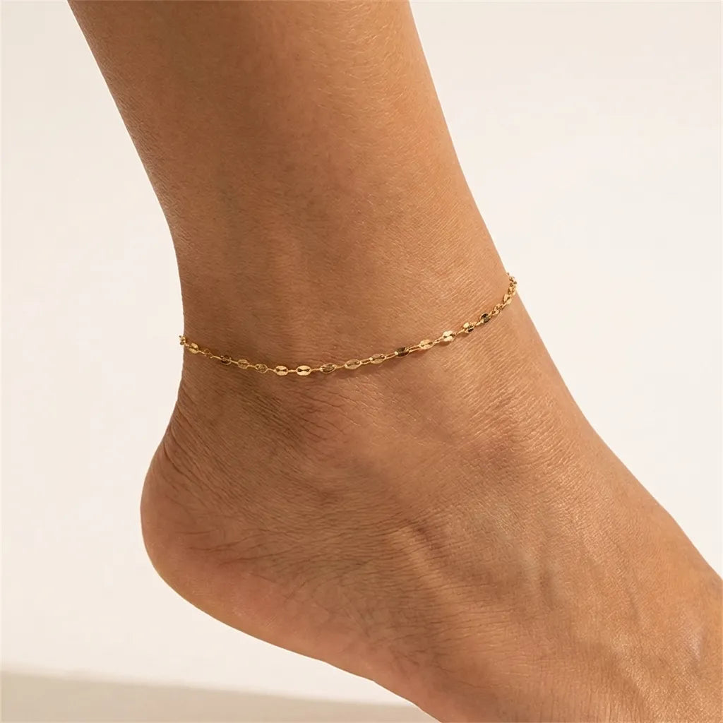 Woman wearing the Charlotte gold chain anklet, flat polished oval links catching the light on the ankle